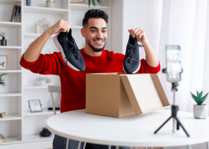 COVID-19 shifts in online shopping behaviours unboxing package new shoes man open package showing new running shoes live stream conduct online video behind the scenes of creator man smiling at camera tripod setting