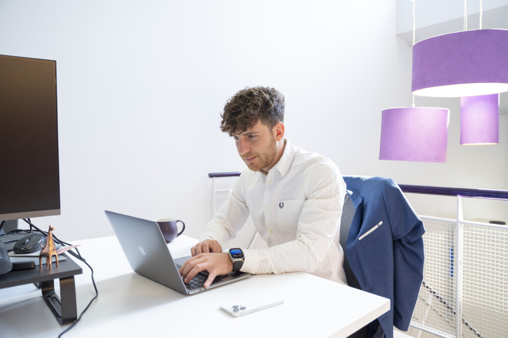 Justin Cuzzocrea, Marketing Co-ordinator sitting at desk working on laptop